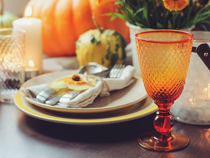 Fall tablescape with stacked plates and silverware and orange colored glassware with pumpkins on a dark Cherrywood table 